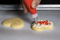 WomanÃ¢â¬â¢s hand piping red frosting onto a heart shaped sugar cookie